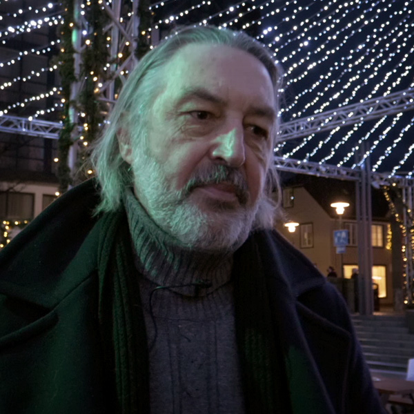 A bearded long haired man looking pensive. Decor lights above him