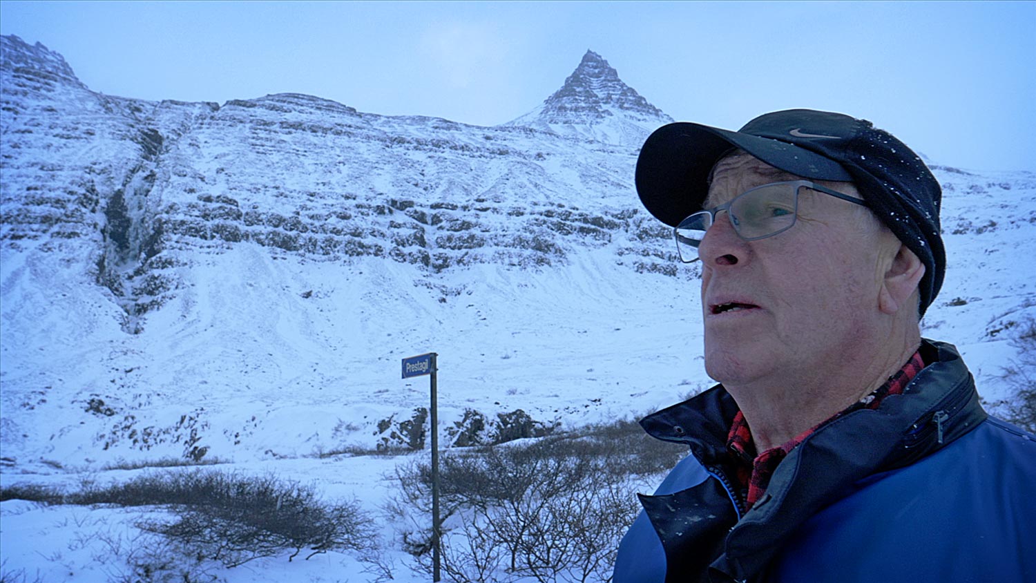 An old man with a cap in a snowy landscape, mountain in the background