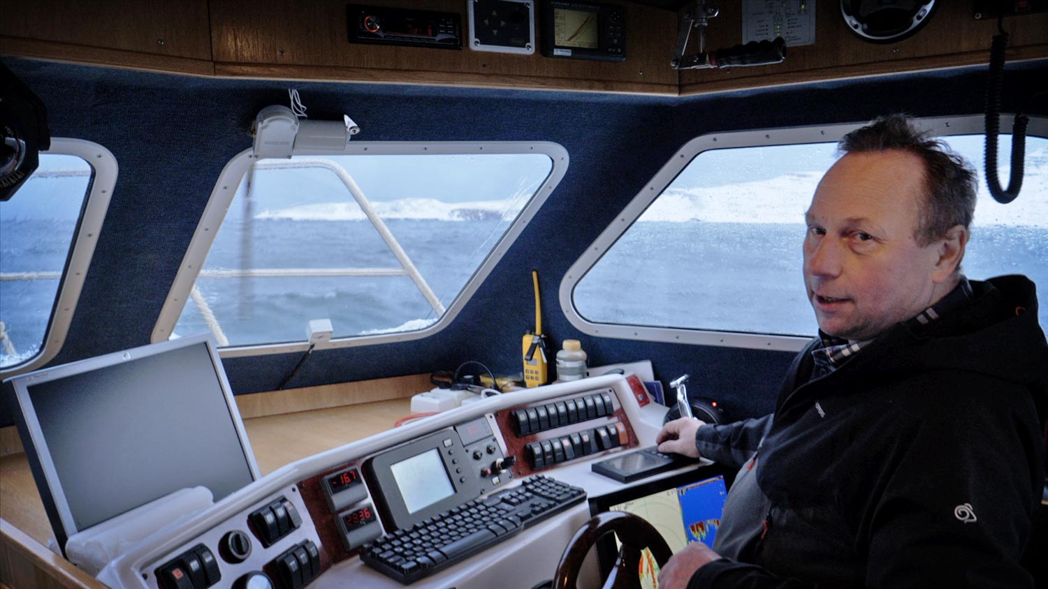 A man driving a motorboat, rough sea and snowy landscape in the background