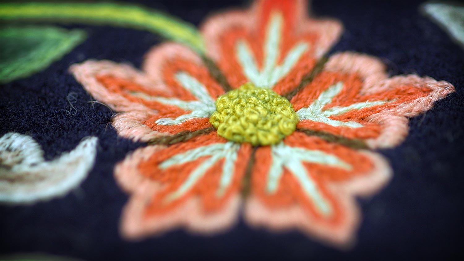 Detail of a multi colored embroidered flower on a dress.