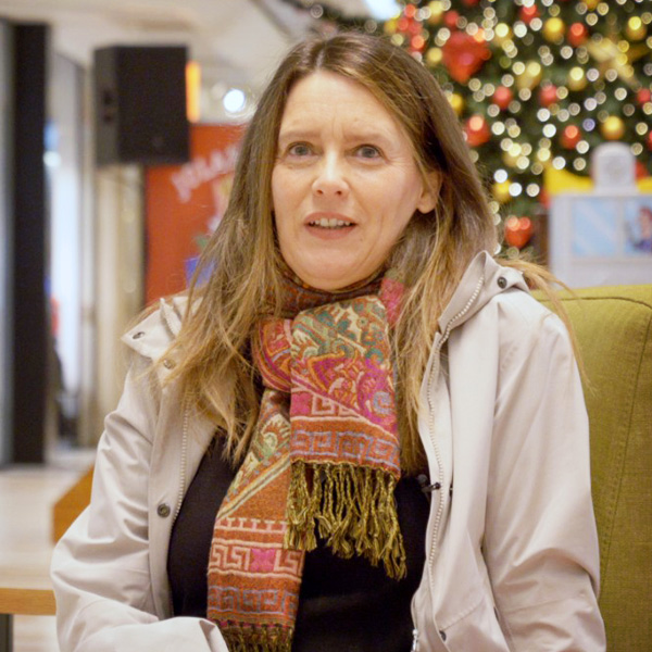 A long haired woman with a scarf with red pattern and in a coat. X-mas tree in the background