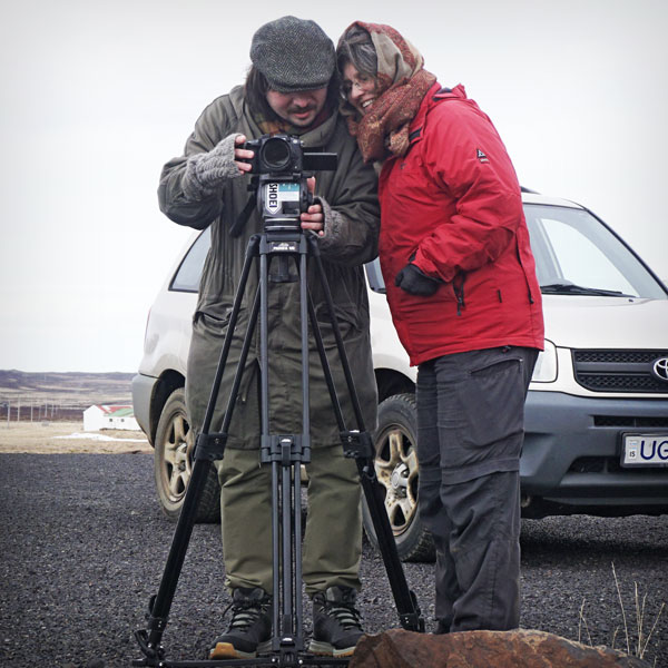 A man and a woman watching something in a camera on a tripod, smiling